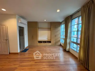 Spacious living room with wooden flooring and large windows offering natural light.