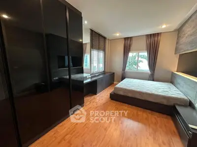 Spacious modern bedroom with sleek black wardrobe and large window view.
