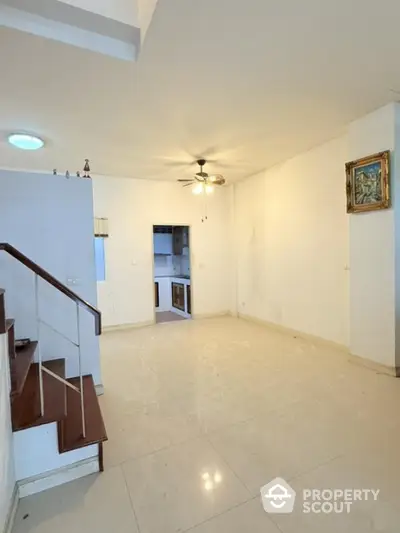 Spacious living room with modern ceiling fan and staircase leading to upper level.