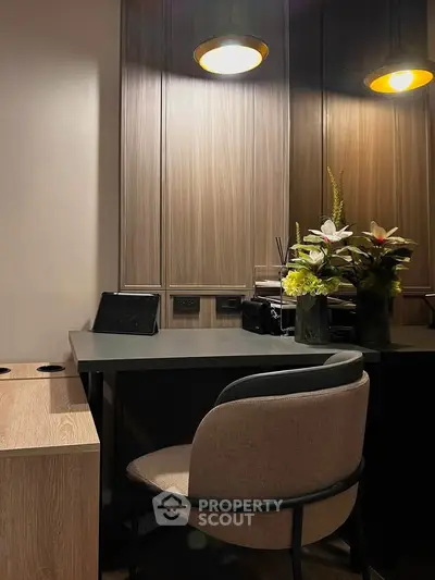 Elegant study area with modern desk, stylish chair, and decorative flowers under warm lighting.