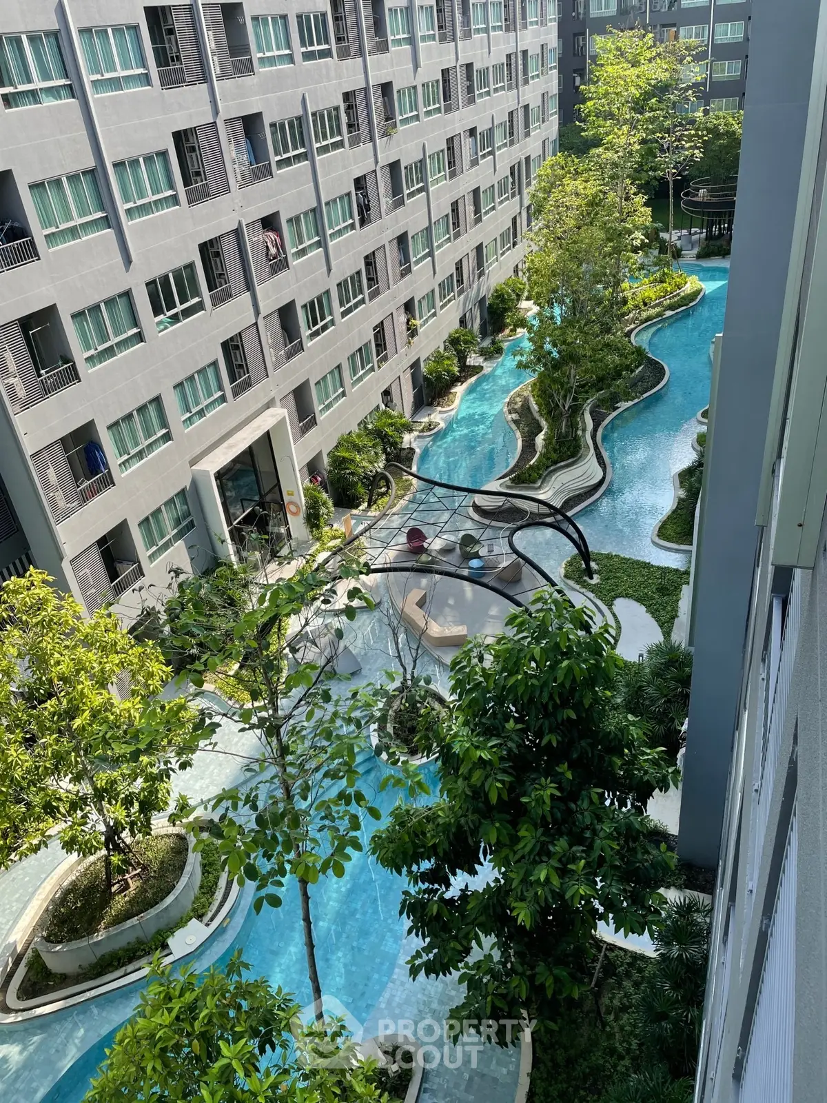 Stunning aerial view of modern apartment complex with lush gardens and winding pool.