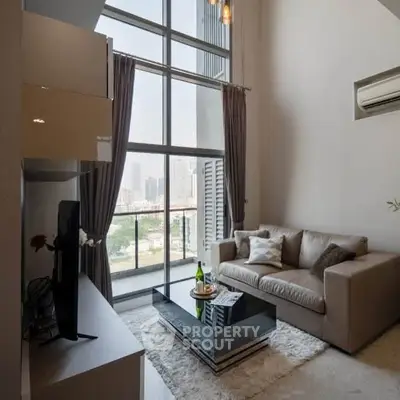 Modern living room with high ceilings and large windows offering city views.