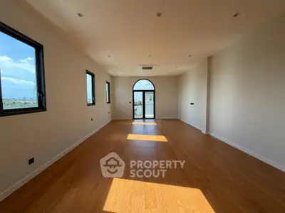 Spacious sunlit room with wooden flooring and large windows offering stunning views.