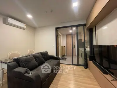 Modern living room with sleek furniture and glass partition leading to kitchen area.