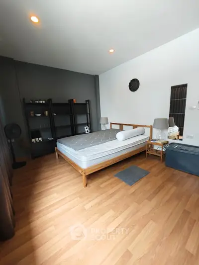 Spacious bedroom with modern decor and wooden flooring, featuring a comfortable bed and stylish shelving.