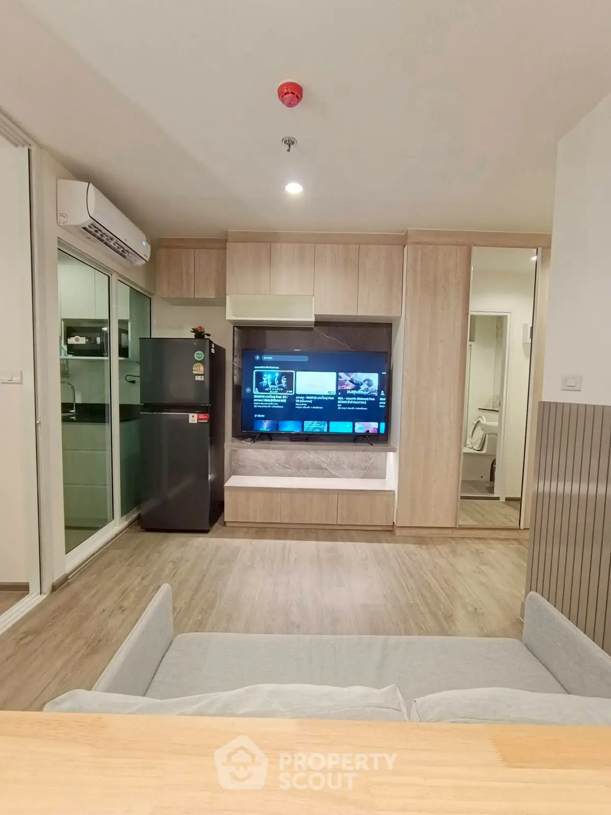 Modern living room with sleek design, featuring a wall-mounted TV, air conditioning, and a compact kitchen area.