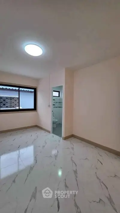 Spacious empty room with marble flooring and natural light, featuring an en-suite bathroom.