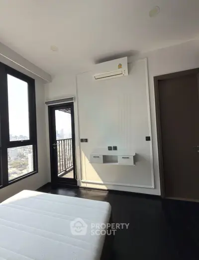 Modern bedroom with city view and balcony access, featuring sleek air conditioning unit and dark wood flooring.