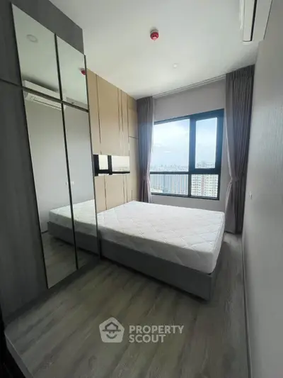 Modern bedroom with large window and mirrored wardrobe, offering a stunning city view.