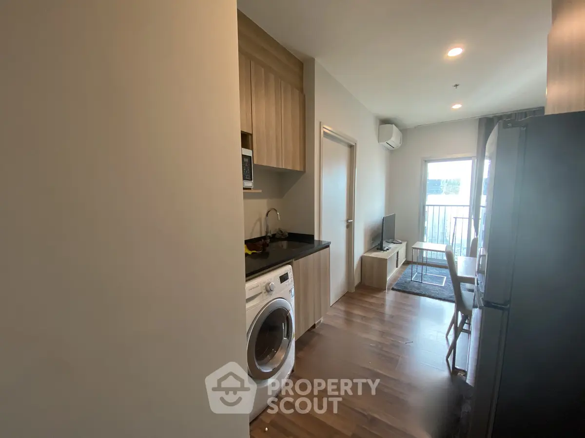 Modern apartment interior with open kitchen and living area, featuring a washing machine and sleek wooden flooring.
