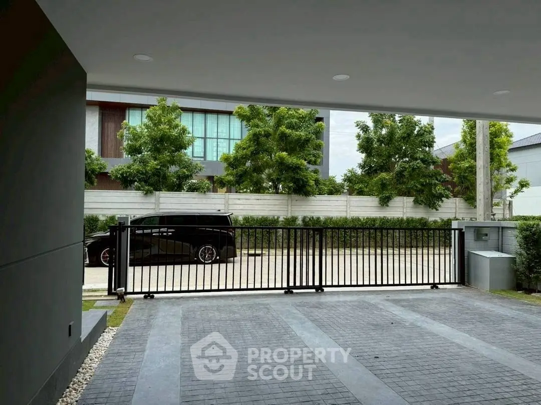 Spacious modern driveway with sleek black gate and lush greenery, perfect for luxury vehicles.