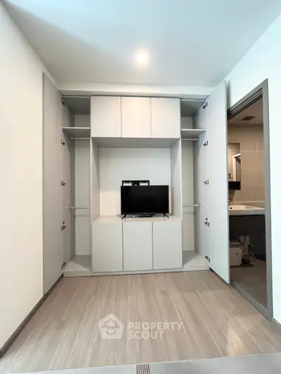 Modern living room with built-in storage and TV, adjacent to a sleek bathroom.