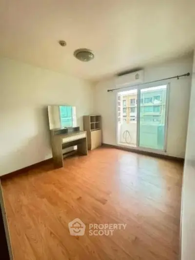Spacious empty bedroom with wooden flooring and large window in modern apartment.