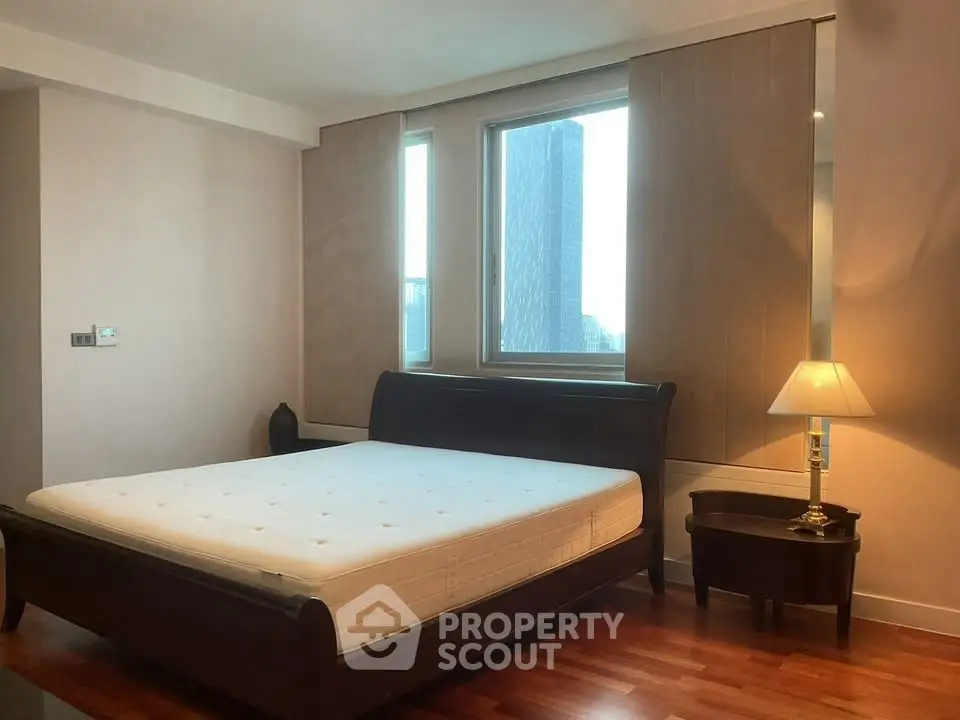 Spacious bedroom with large windows and elegant wooden furniture in a modern apartment.