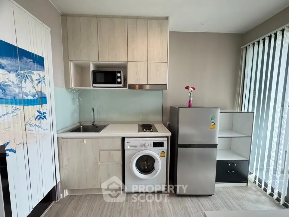 Modern compact kitchen with washing machine, microwave, and fridge in a stylish apartment.