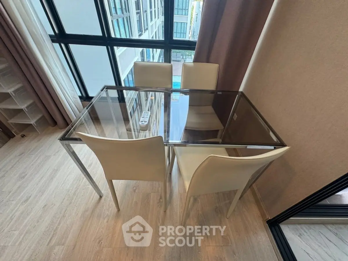 Modern dining area with glass table and white chairs in a high-rise apartment.