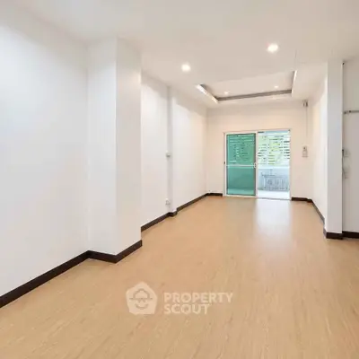 Spacious empty room with wooden flooring and large window, perfect for customization.