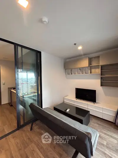 Modern living room with sleek furniture and TV, featuring a sliding glass door and wooden flooring.