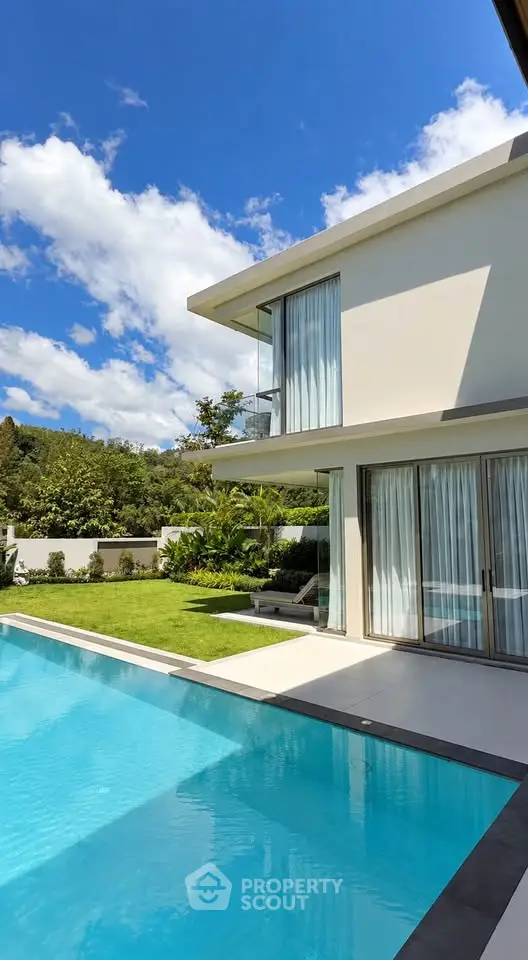 Luxurious modern home with a stunning pool and lush garden under a clear blue sky.