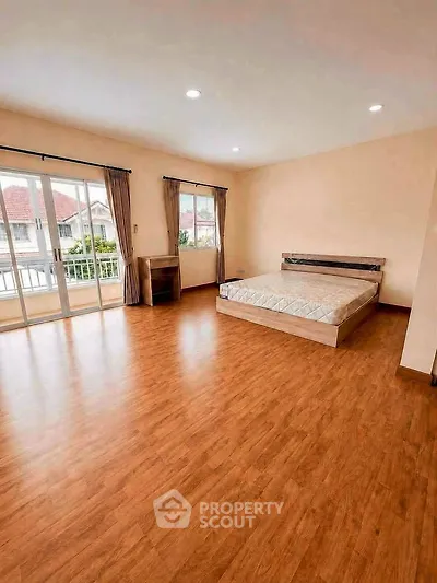 Spacious bedroom with wooden flooring and large windows offering natural light and a view.