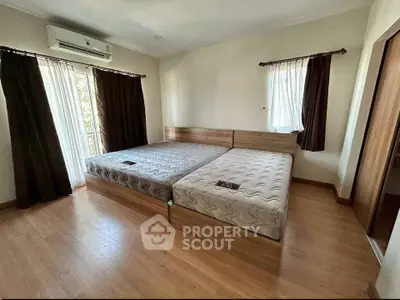 Spacious bedroom with twin beds and natural light, featuring wooden flooring and modern air conditioning.
