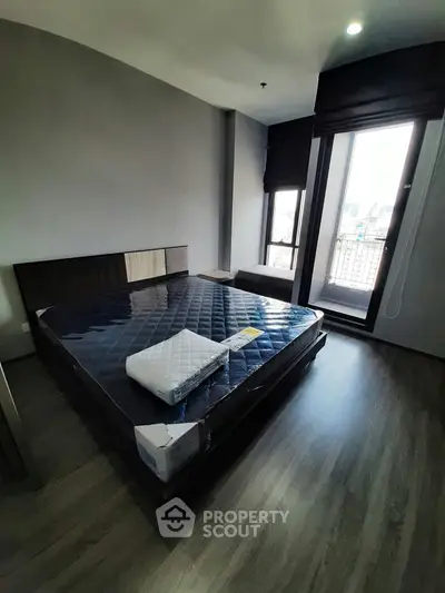 Modern bedroom with large window and city view, featuring a new mattress on wooden flooring.