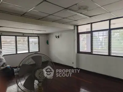 Spacious room with large windows and ceiling fan, ideal for renovation.