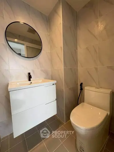 Modern bathroom with sleek vanity and round mirror, featuring elegant tile design.