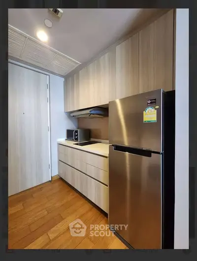 Modern kitchen with sleek cabinetry and stainless steel fridge in a cozy apartment.