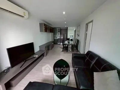 Modern living room with sleek furniture and open layout, featuring a large TV and dining area.