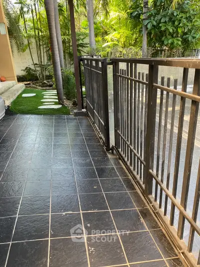 Charming garden view from a spacious balcony with elegant black tiles and lush greenery.