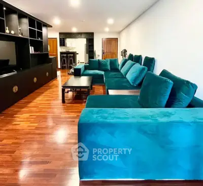 Spacious living room with elegant teal sofa and wooden flooring, perfect for modern living.