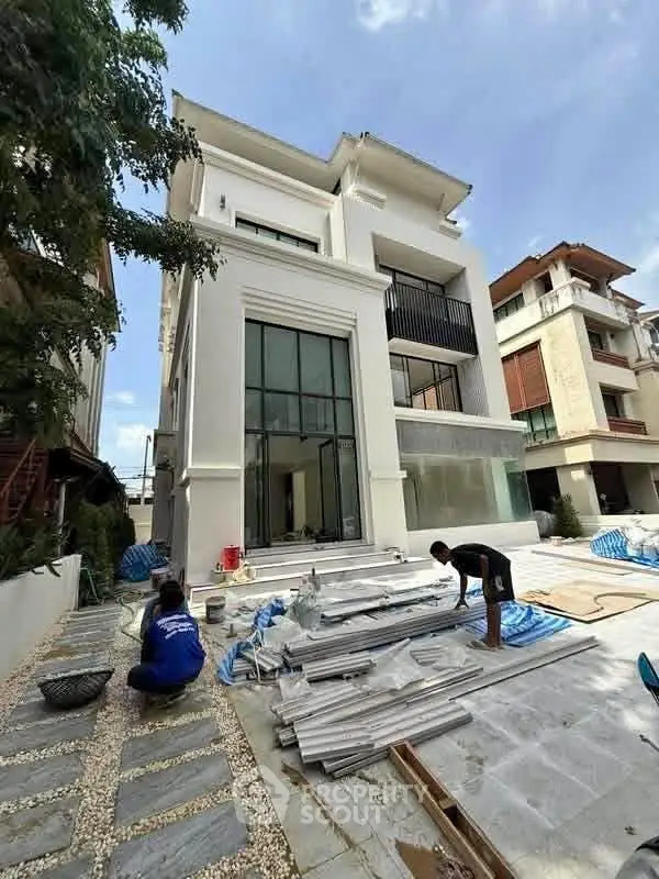 Modern three-story house under construction with large windows and spacious outdoor area.