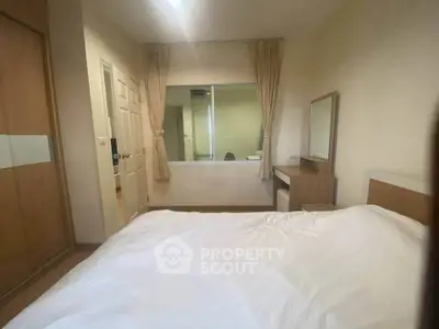 Cozy bedroom with large bed, wooden wardrobe, and dressing table in a well-lit apartment.