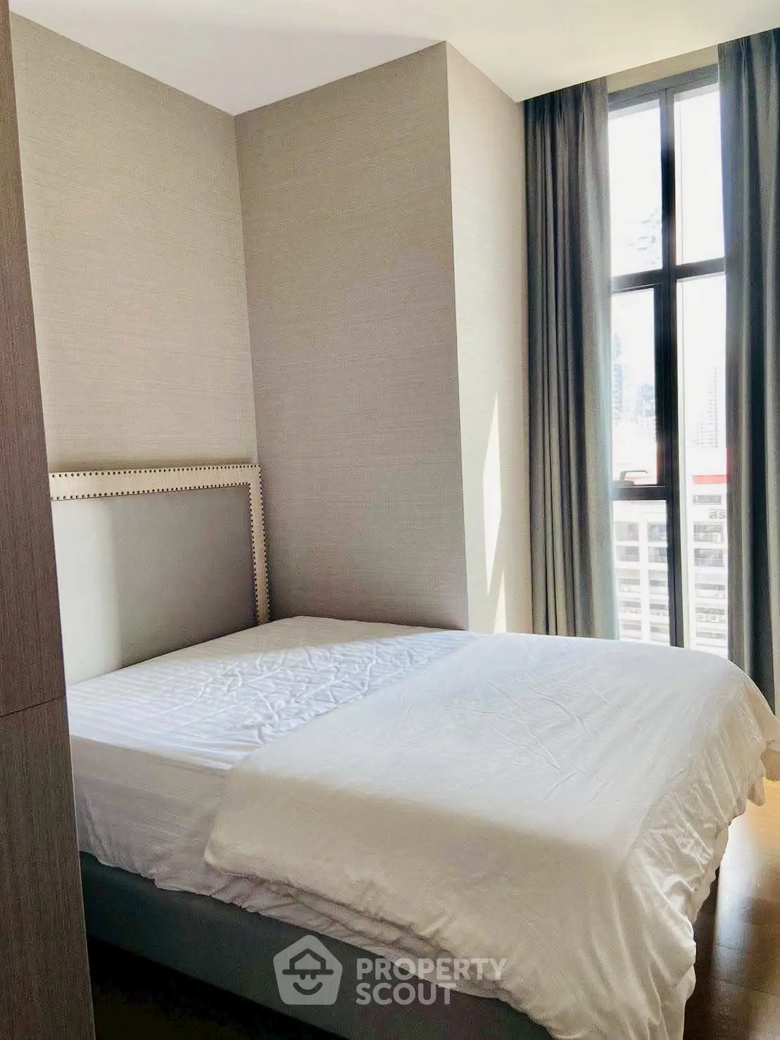 Modern bedroom with large window and elegant decor in urban apartment.