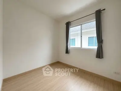 Spacious empty bedroom with wooden flooring and large window, perfect for customization.