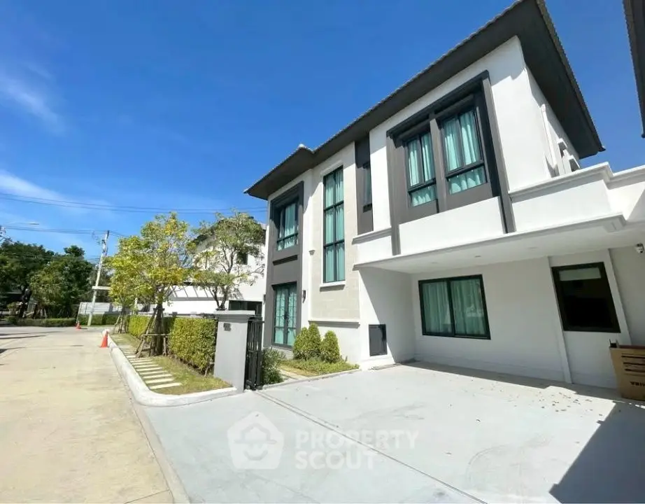 Modern two-story house with large windows and driveway in a sunny neighborhood.