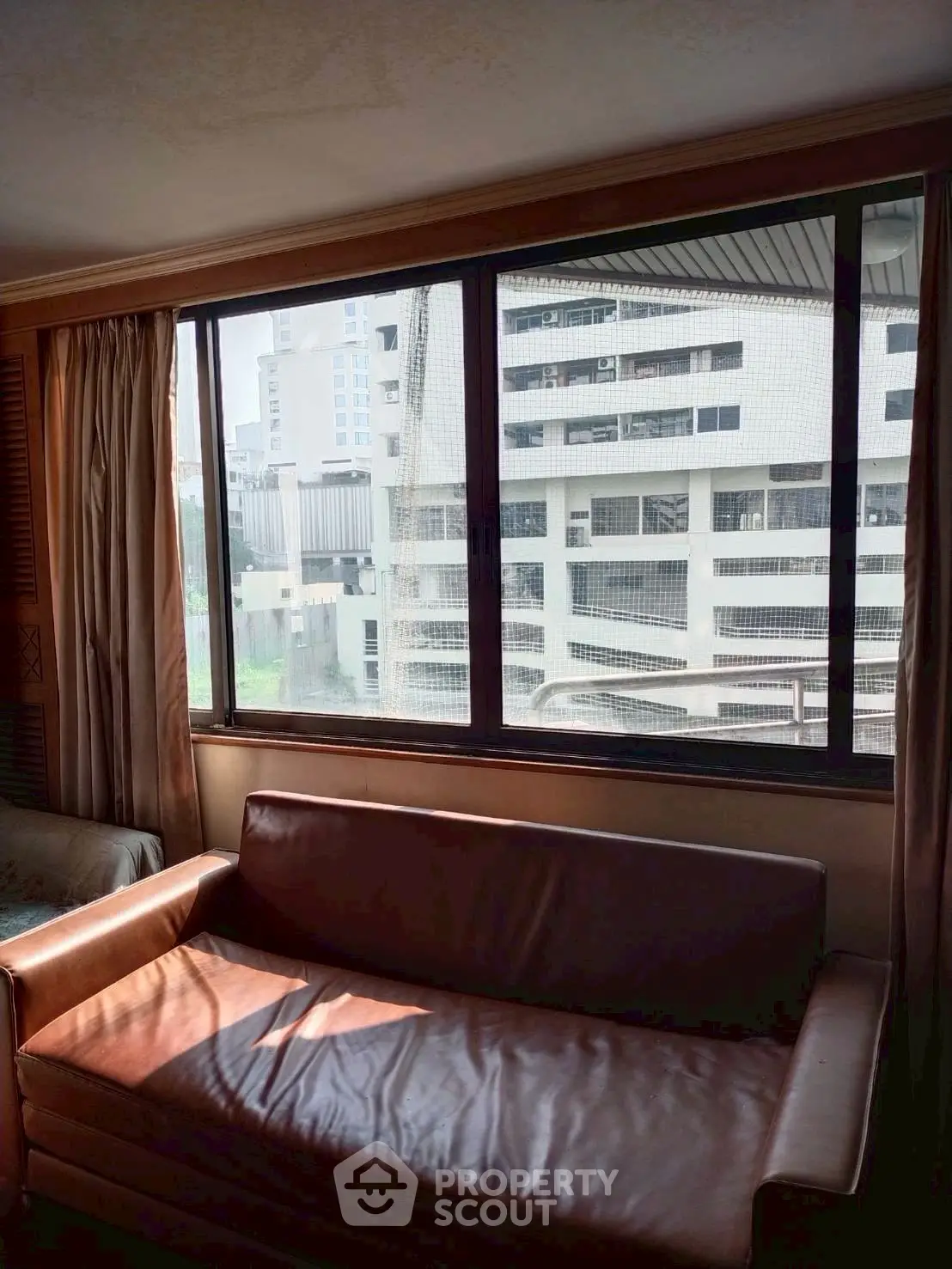 Cozy living room with leather sofa and large window view of urban buildings.