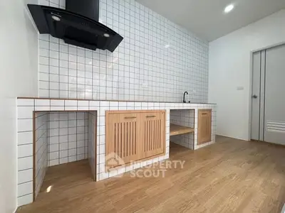 Modern kitchen with tiled backsplash and wooden cabinets, featuring a sleek black range hood.