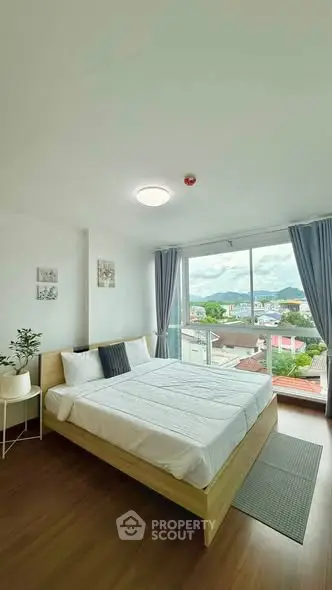 Bright bedroom with large window offering stunning city view, modern decor, and cozy ambiance.