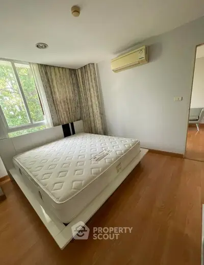 Spacious bedroom with large window and air conditioning, featuring a comfortable mattress and wooden flooring.