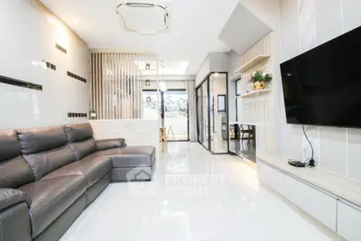 Modern living room with sleek design and spacious layout, featuring a large leather sofa and wall-mounted TV.