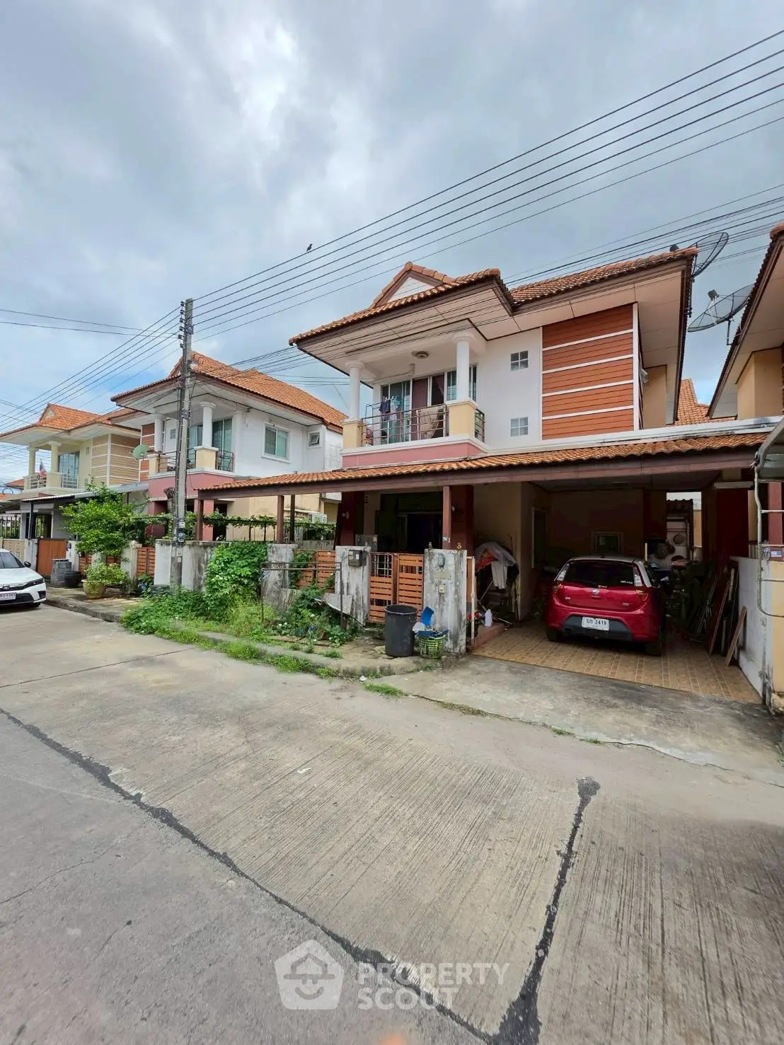 Charming two-story house with carport in a suburban neighborhood, featuring a tiled roof and a small front garden.