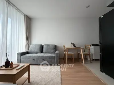 Modern living room with sleek gray sofa and dining area, featuring natural light and minimalist decor.