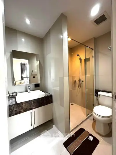 Modern bathroom with glass shower and sleek vanity in contemporary apartment.