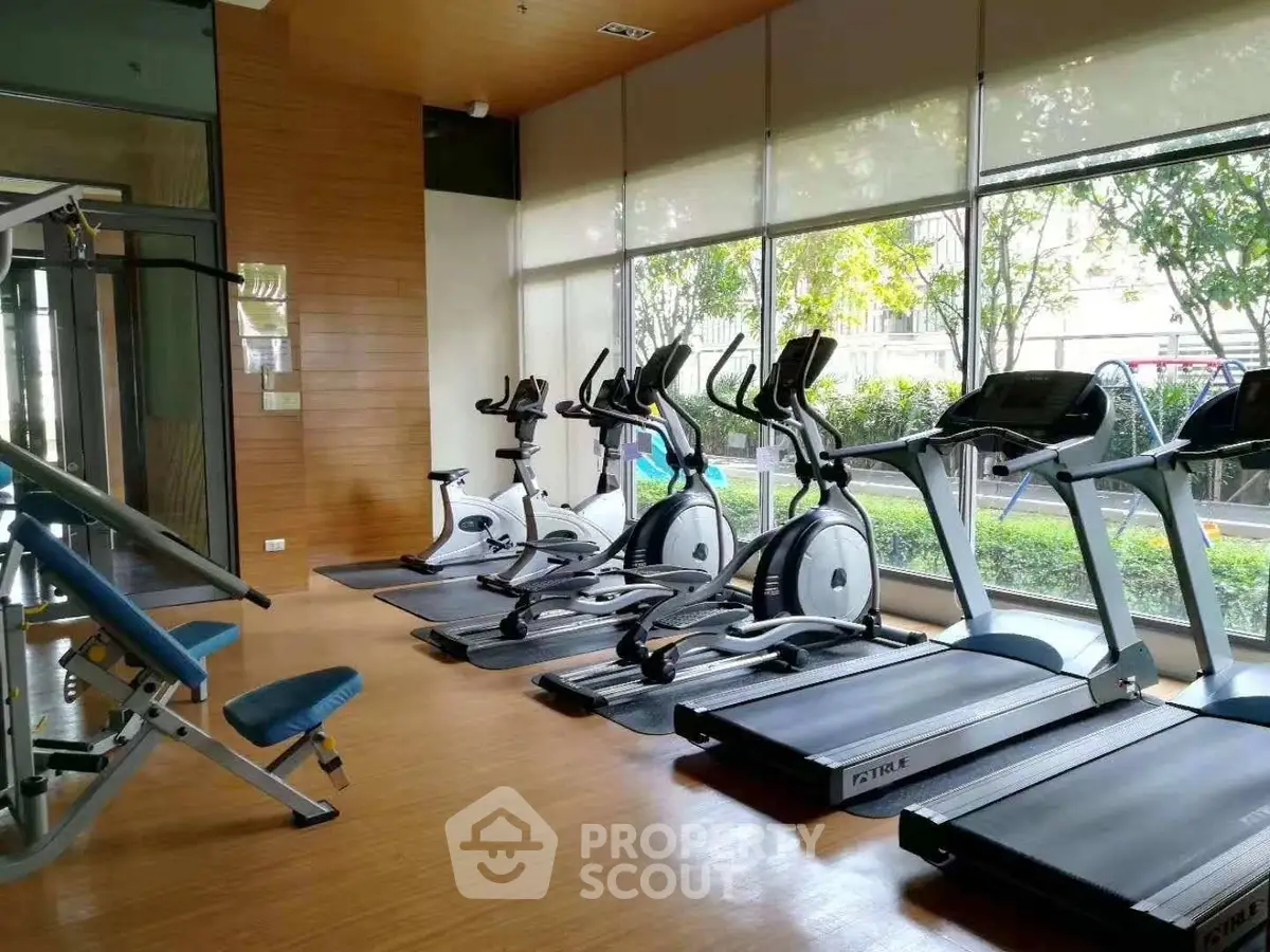 Modern gym with cardio equipment and large windows in residential complex.