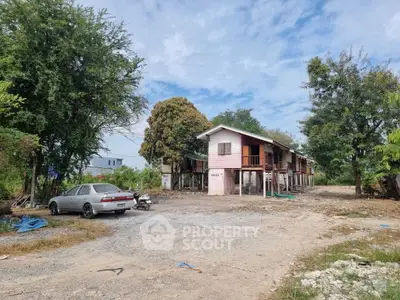 Rural property with two-story house and spacious outdoor area, surrounded by trees and open sky.