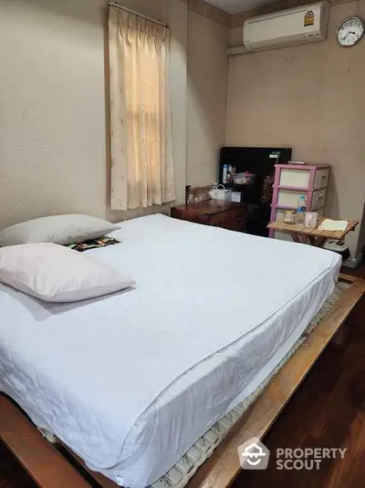 Cozy bedroom with wooden flooring and air conditioning, featuring a comfortable bed and ample natural light.