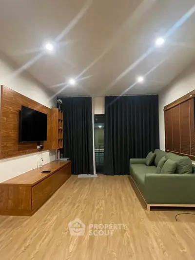 Modern living room with wooden flooring, green sofa, and wall-mounted TV for a cozy ambiance.