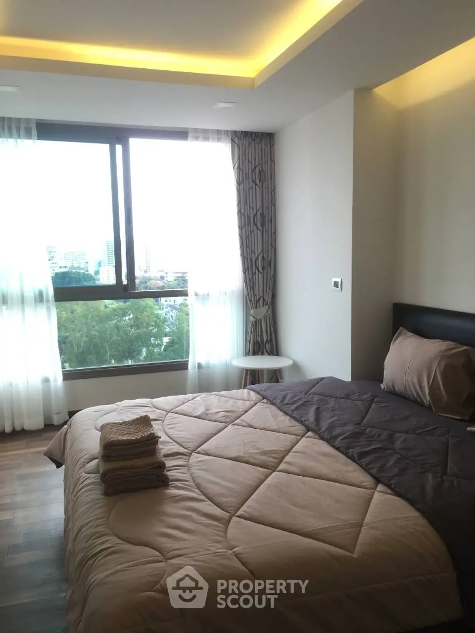 Modern bedroom with large window and cozy bedding in a high-rise apartment.
